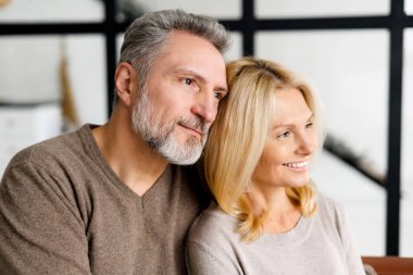 Orta yaşlı eşler evdeki kanepede oturur ve bir tarafa bakarlar.