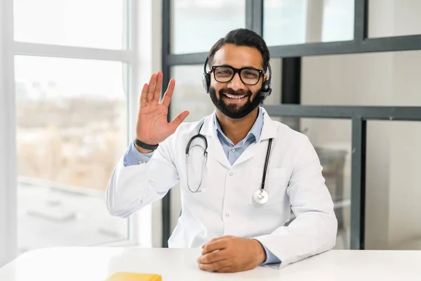 Indiano medico maschio in abito bianco indossare auricolare parlando con paziente a distanza — Foto Stock