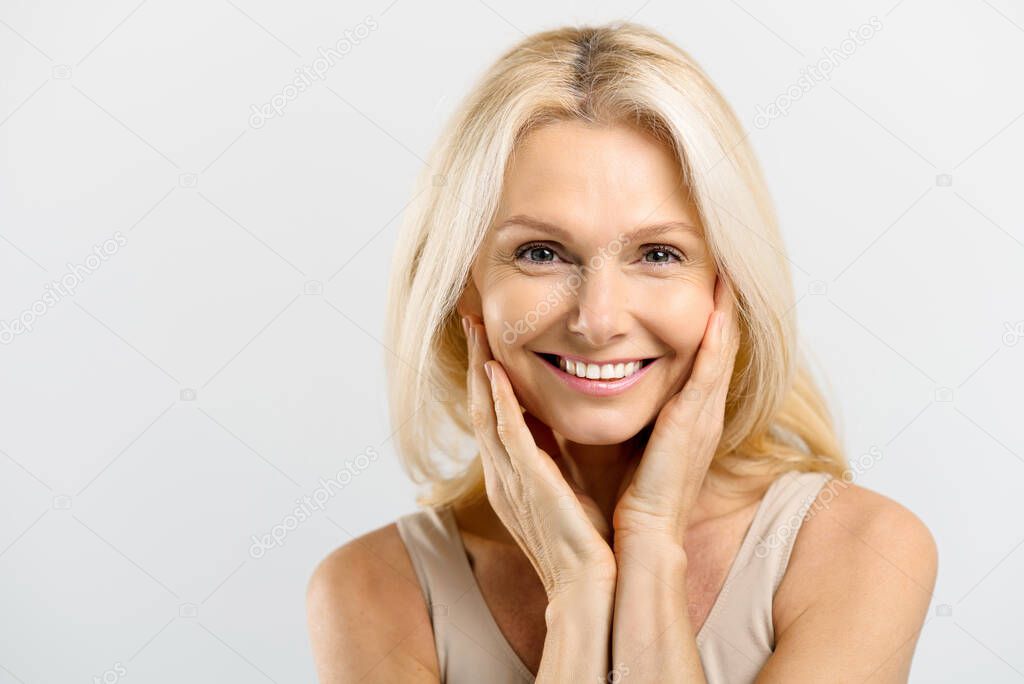 Enchanting middle-aged woman with blonde hair hug herself and look at the camera