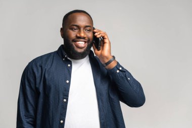 Aşırı neşeli Afro-Amerikalı adam gri arka planda akıllı telefonla konuşuyor.