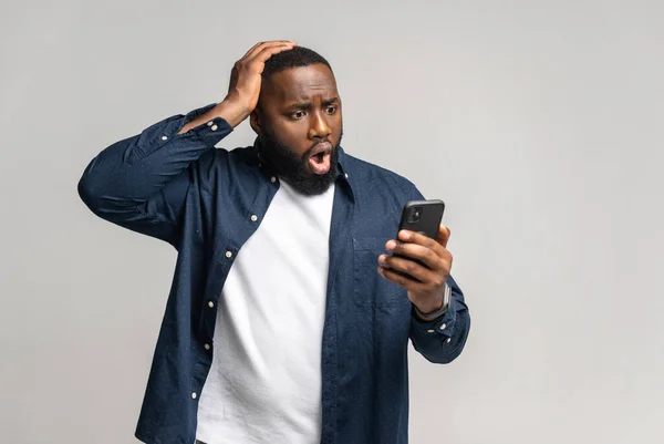 Chico afroamericano sorprendido mirando el teléfono inteligente sosteniendo la cabeza en la desesperación — Foto de Stock