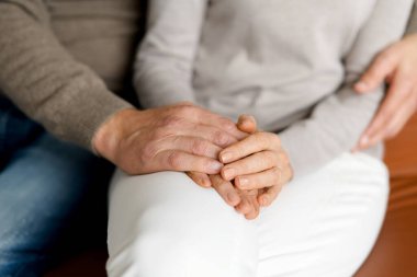 Orta yaşlı çiftin el ele tutuşup el ele oturduğu yakın plan bir fotoğraf.