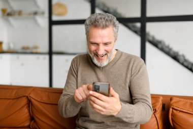 Neşeli, sırıtan, gri saçlı, sıradan giysili adam. Akıllı telefona bak.