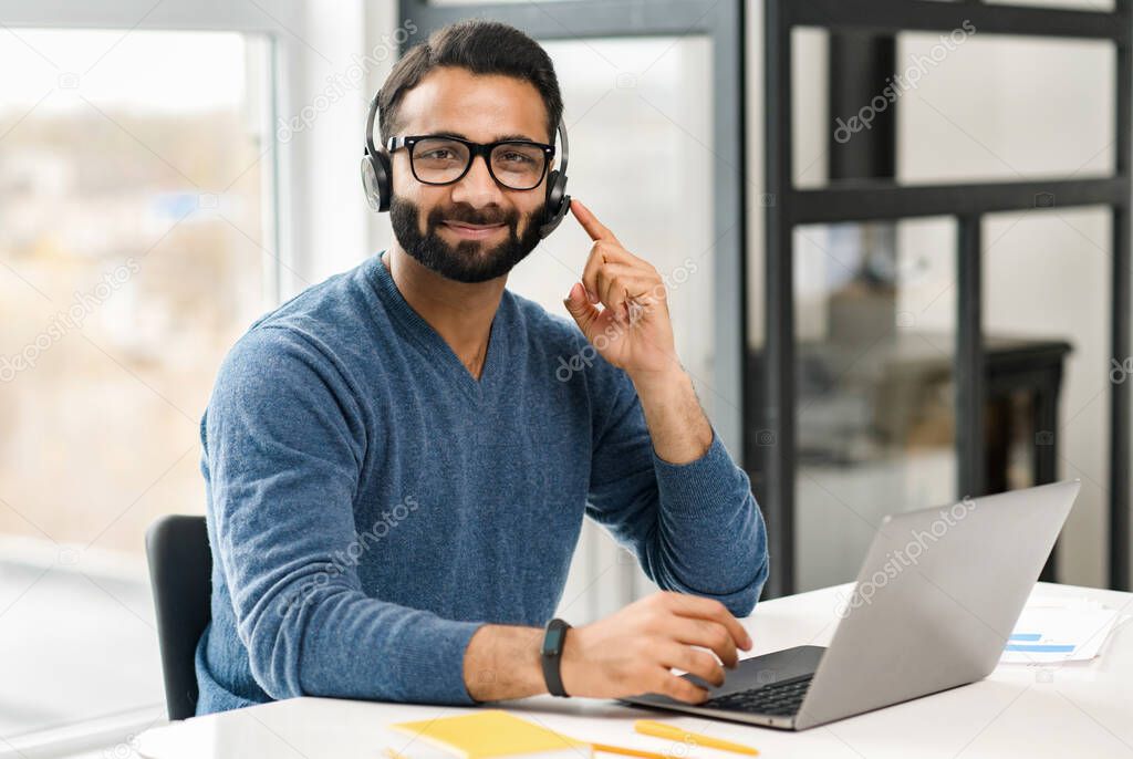Helpful and smiling Indian male employee wearing headset and eyeglasses