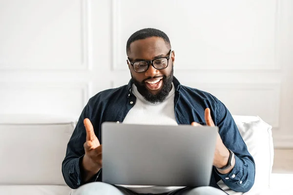 Pozitivní afroameričan pomocí notebooku pro videohovory sedí na pohovce doma — Stock fotografie