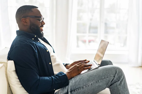 Vista lateral en el joven afroamericano moderno freelancer chico usando el ordenador portátil — Foto de Stock