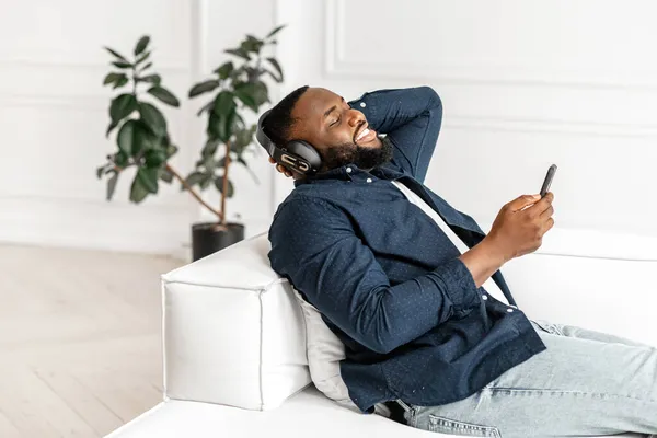 Hombre afroamericano joven con camisa casual sentado en sofá blanco —  Fotos de Stock