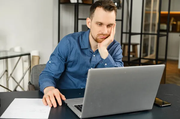 Verveelde jonge mannelijke ondernemer werkt aan het project online op de laptop — Stockfoto