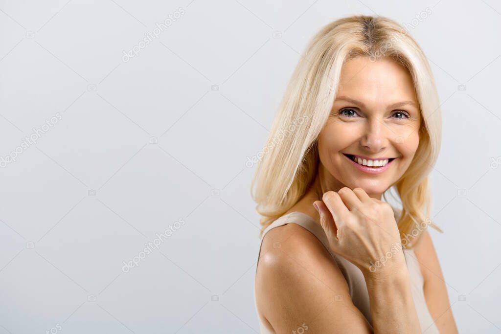 Middle-aged attractive blonde woman gently touching face and laughing