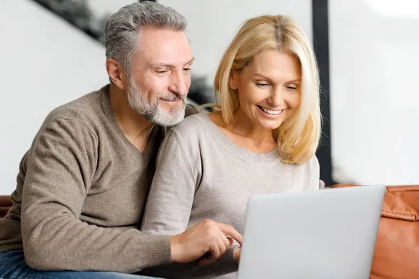 Middelbaar stel zit op de bank en kijkt naar het scherm — Stockfoto