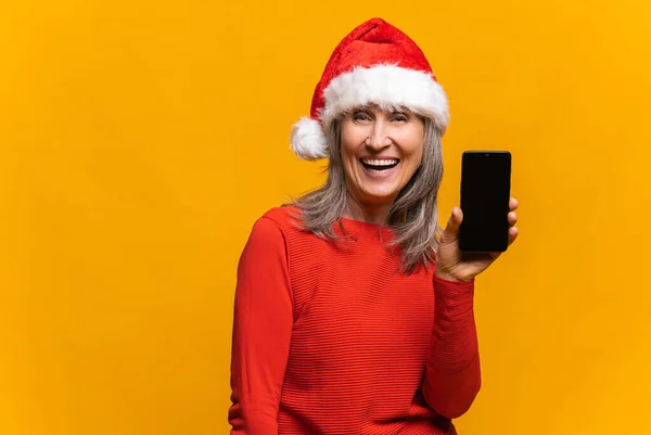 Zachwycona kobieta w kapeluszu Santa trzymając smartfona z pustym ekranem — Zdjęcie stockowe