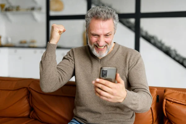 Senior hombre de pelo gris está utilizando el teléfono inteligente para ver partidos de fútbol deportivo —  Fotos de Stock