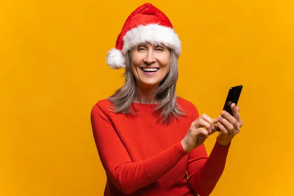 Gros plan portrait de femme âgée hilarante en chapeau de Père Noël à l'aide d'un smartphone — Photo