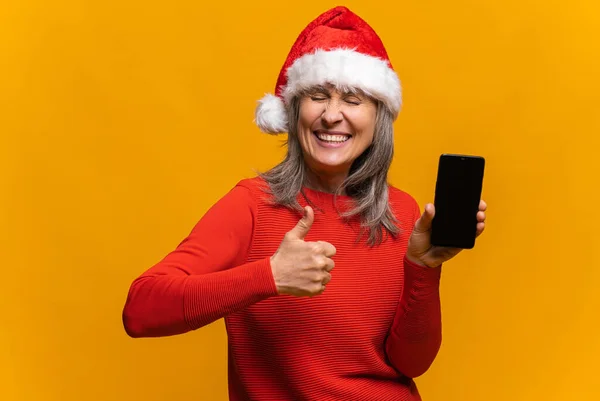 Zabawna seniorka w kapeluszu Santa trzymająca smartfona z pustym ekranem — Zdjęcie stockowe