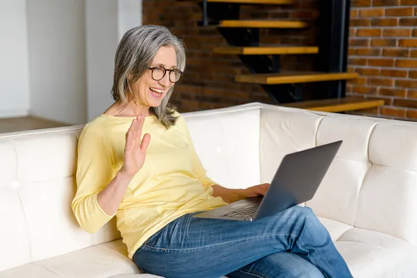 Весела впевнена старша жінка використовує ноутбук для відеозв'язку — стокове фото