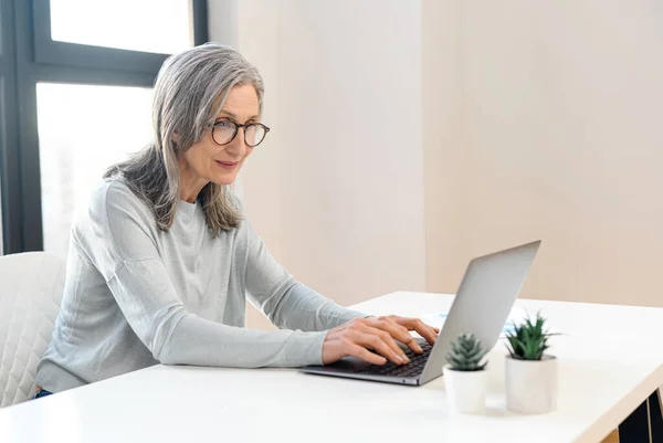 Gözlüklü, olgun bir iş kadını dizüstü bilgisayar kullanıyor. — Stok fotoğraf