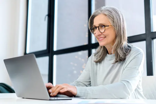Veselá obchodní dáma s brýlemi na klávesnici, dívá se na obrazovku spokojeně — Stock fotografie