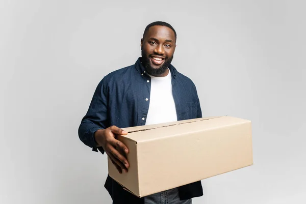 Glad ung afro-amerikansk man som håller i pappkartong, ler och tittar på kameran — Stockfoto