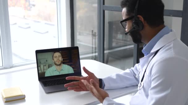 Médico masculino indio que utiliza el ordenador portátil para la reunión en línea con el paciente, escucha las quejas — Vídeos de Stock