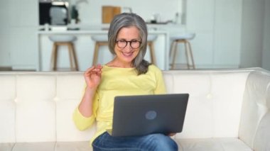 Video bağlantısı için dizüstü bilgisayar kullanan neşeli, kendinden emin yaşlı bir kadın.