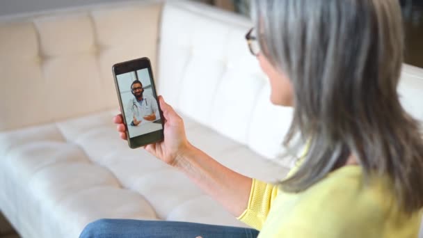 Senior donna matura si siede sul divano a casa facendo videochiamata al medico — Video Stock
