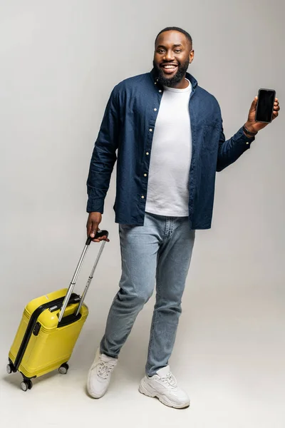 Hombre africano feliz de pie con pequeño bolso elegante y teléfono celular en sus manos — Foto de Stock