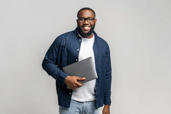 Manlig entreprenör står i studio isolerad på grå och bär trendiga laptop — Stockfoto