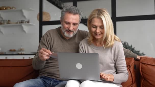 Veselý pár středního věku sleduje na obrazovce notebooku a kontroluje číslo kreditní karty — Stock video