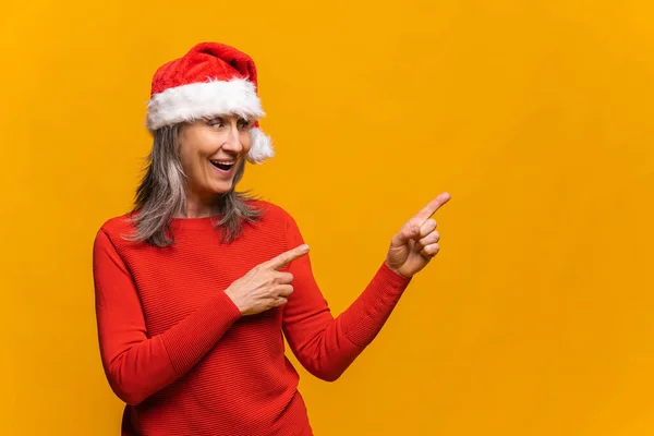 Mulher positiva em vermelho Papai Noel olha e aponta para o lado com ambos os dedos indicadores — Fotografia de Stock