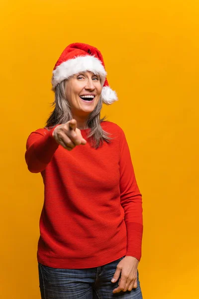 Alegre feliz sênior mulher no santa chapéu aponta indicador dedo para a câmera e ri — Fotografia de Stock