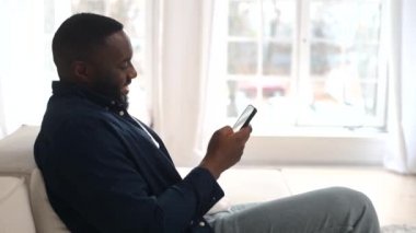Çekici bin yıllık sakallı Afro-Amerikalı adam rahat koltukta oturuyor.