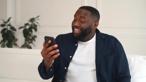 Pozytywny afro-amerykański facet z zębaty uśmiech za pomocą smartfona do połączenia wideo — Wideo stockowe