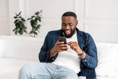 Heyecanlı genç Afro-Amerikan sakallı adam akıllı telefon kullanıyor.