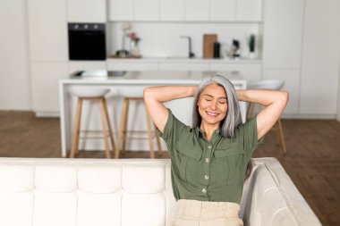 Serene kaygısız orta yaşlı kadın, koltukta oturan uzun gri saçlı.