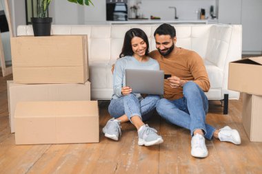 Neşeli genç Hintli çift yeni daireye taşınıp internetten alışveriş yapıyor.
