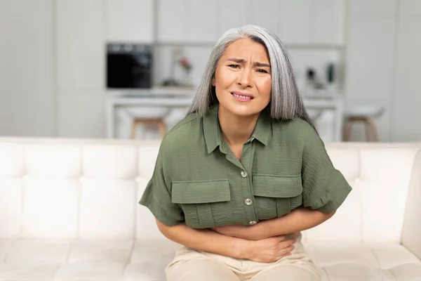Concerned mature 50s woman with gray-hair suffering from stomach-ache