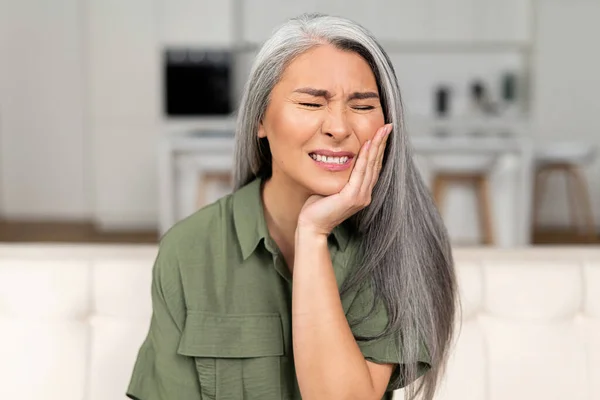 Стурбована зріла 50-річна жінка з сірим волоссям відчуває сильний зубний біль — стокове фото