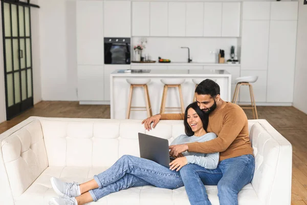 Pareja alegre en el amor pasar el tiempo libre en línea con un ordenador portátil en casa. Mujer joven y hombre mirando la pantalla del ordenador portátil mientras está sentado en el sofá, viendo películas de comedia —  Fotos de Stock