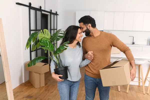 젊은 다 인종 남편 과 아내가 화분에 식물을 담은 판지 상자를 들고 있는 것을 흉내낸다. 좋은 집, 새 아파트로 이사 한 부부는 자기 집으로 이사한다 — 스톡 사진