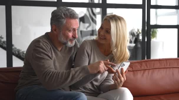 Gelukkig senior paar met smartphone op de bank besteedt vrije tijd — Stockvideo