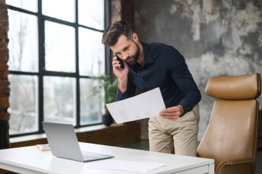 Modern çatı katında dururken akıllı telefondan konuşan konsantre erkek küçük işletme sahibi. Gündelik kıyafet bekleme programında başarılı bir çağdaş adam yöneticisi.