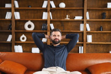 Röportajda. Deri koltukta oturan ve gülümseyen bir adam, arka planda kitaplıkla rahatlık ve rahatlık hisseder.