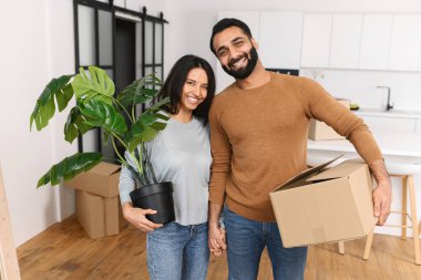 Birlikte yeni bir daireye taşınırken kameraya bakan genç bir çift. Güzel bir ev, yeni bir daireye taşınmak, evli bir çift kendi evine taşınmak demek.