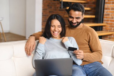 Neşeli Hintli çift dizüstü bilgisayarda seyrediyor ve dişlek gülümsüyor. Kocasıyla online alışveriş yaparken çok mutlu bir kadın. Para transferi, online bankacılık