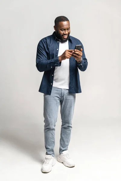 Glädjefylld och bekymmerslös afroamerikansk man med smartphone isolerad på grå — Stockfoto