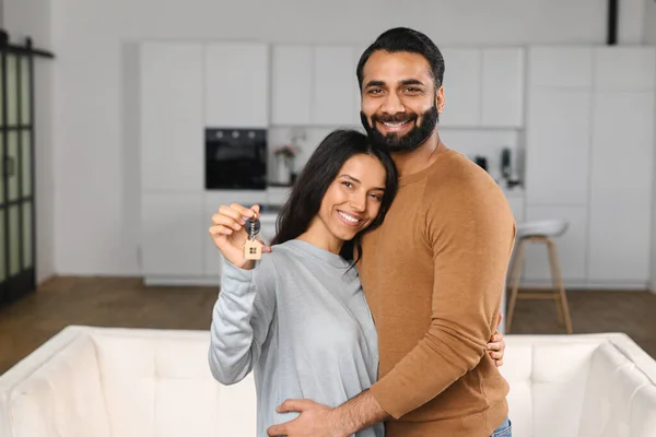 Feliz pareja de la familia india mostrando nuevas llaves de la casa a la cámara mientras posan en interiores. Propia casa, propiedad inmobiliaria y vivienda. Hipoteca y apartamento —  Fotos de Stock