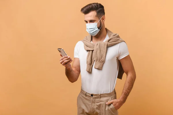 Портрет концентрированного человека в защитной маске с помощью смартфона, во время чтения чего-то, наслаждающегося мобильным приложением. Человек смотрит на экран устройства — стоковое фото
