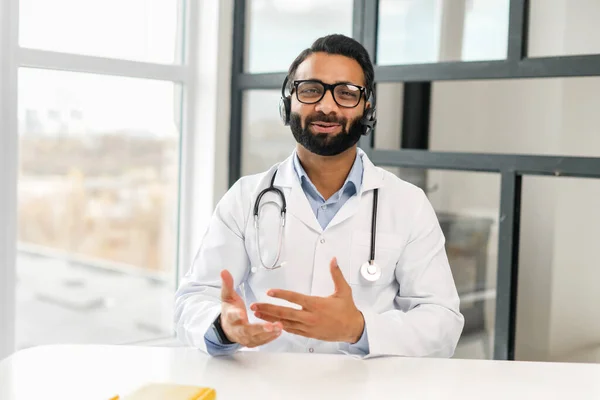 MD maschio indiano indossando auricolari, occhiali e abito medico rendendo consultazione online — Foto Stock