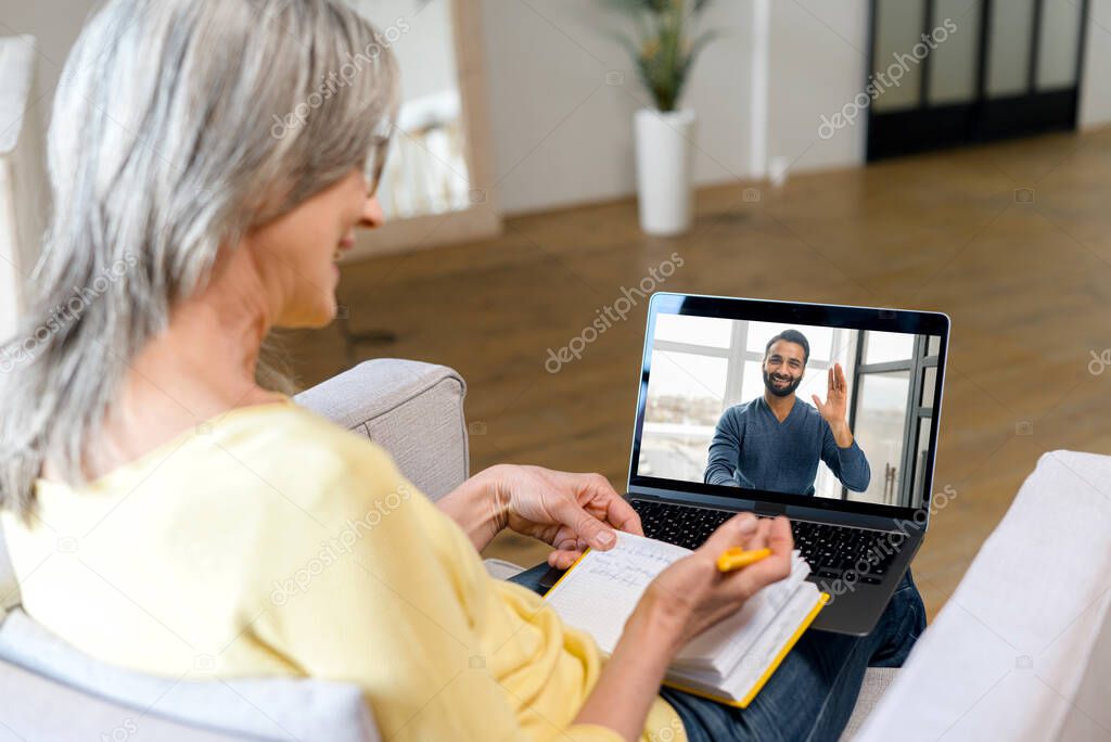 Smiling senior woman talking online with young Indian man on the laptop screen