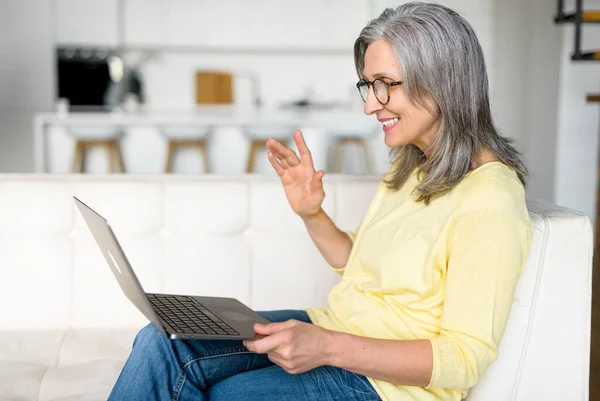 A boldog végzős nőnek videohívása van a laptopon, ahogy otthon ül a kanapén. — Stock Fotó